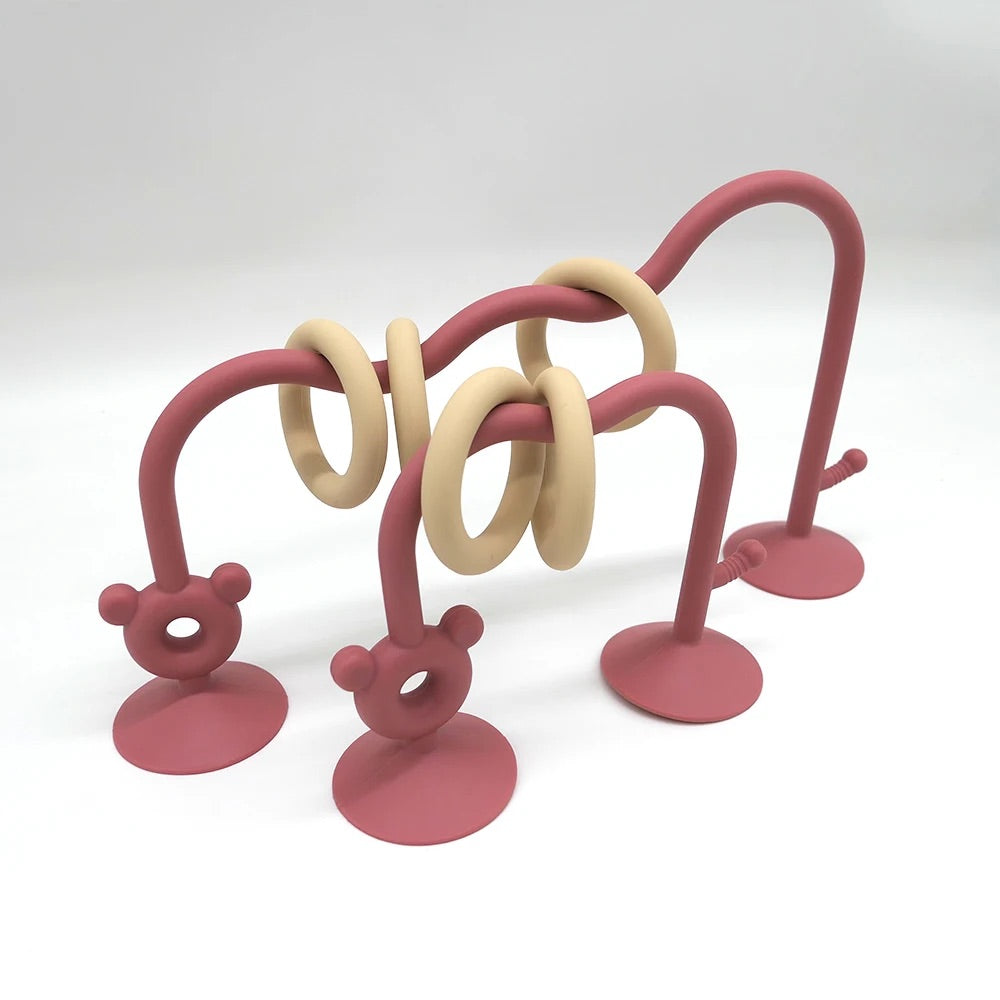 Reddish pink silicone bead maze toy for babies with suction cups and sliding rings.