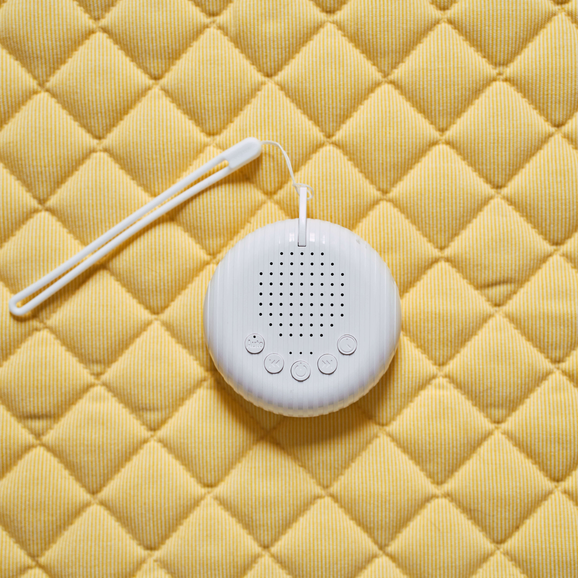 Portable baby white noise machine with hanging strap on yellow quilted background