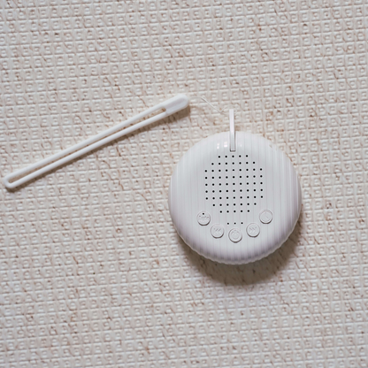 Compact white noise machine for babies placed on soft neutral fabric surface