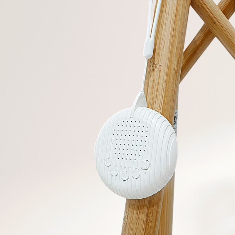 Lightweight baby white noise machine hanging from wooden stand using flexible strap