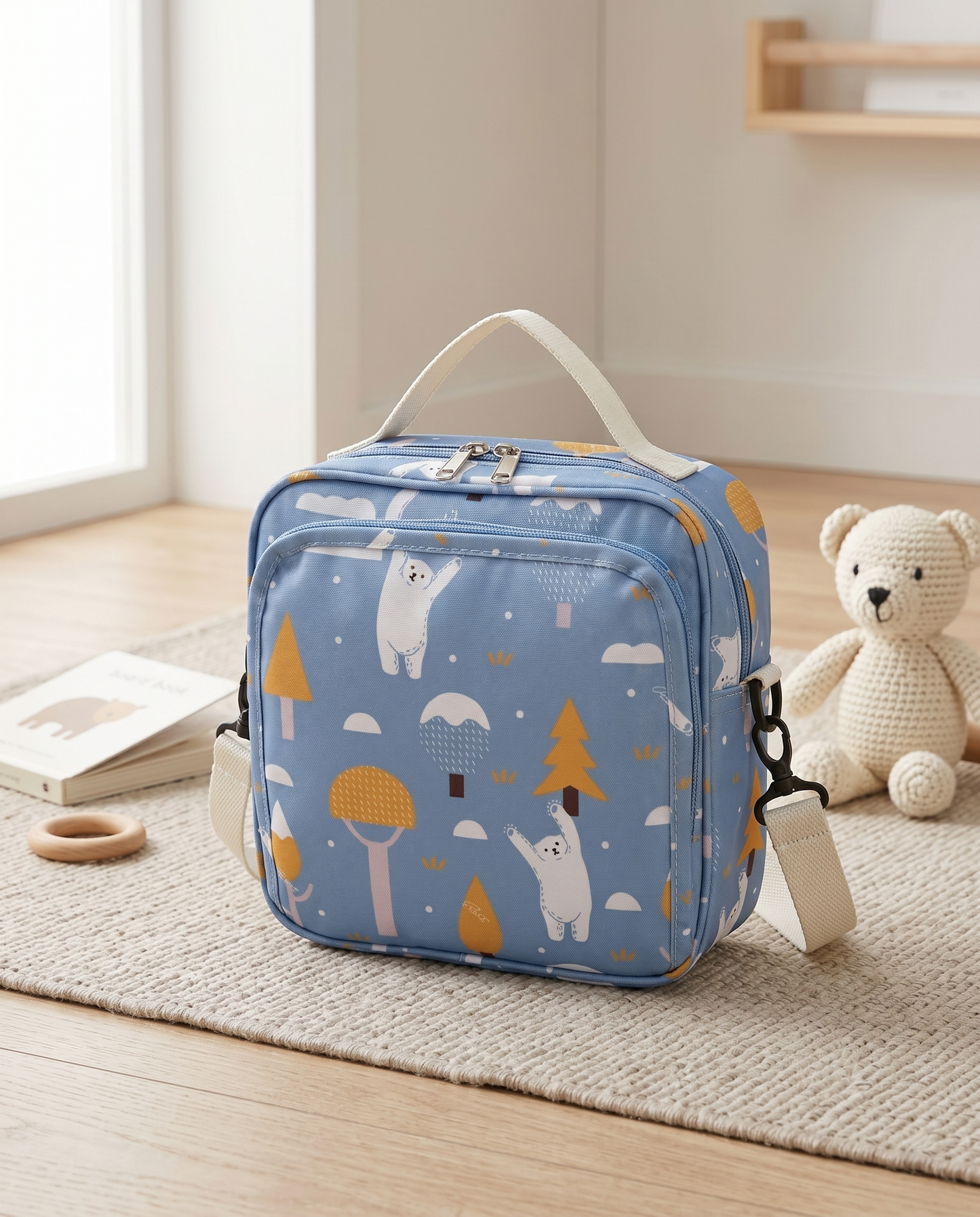 Blue nappy bag bear print with top handle and crossbody strap styled with teddy bear on nursery rug